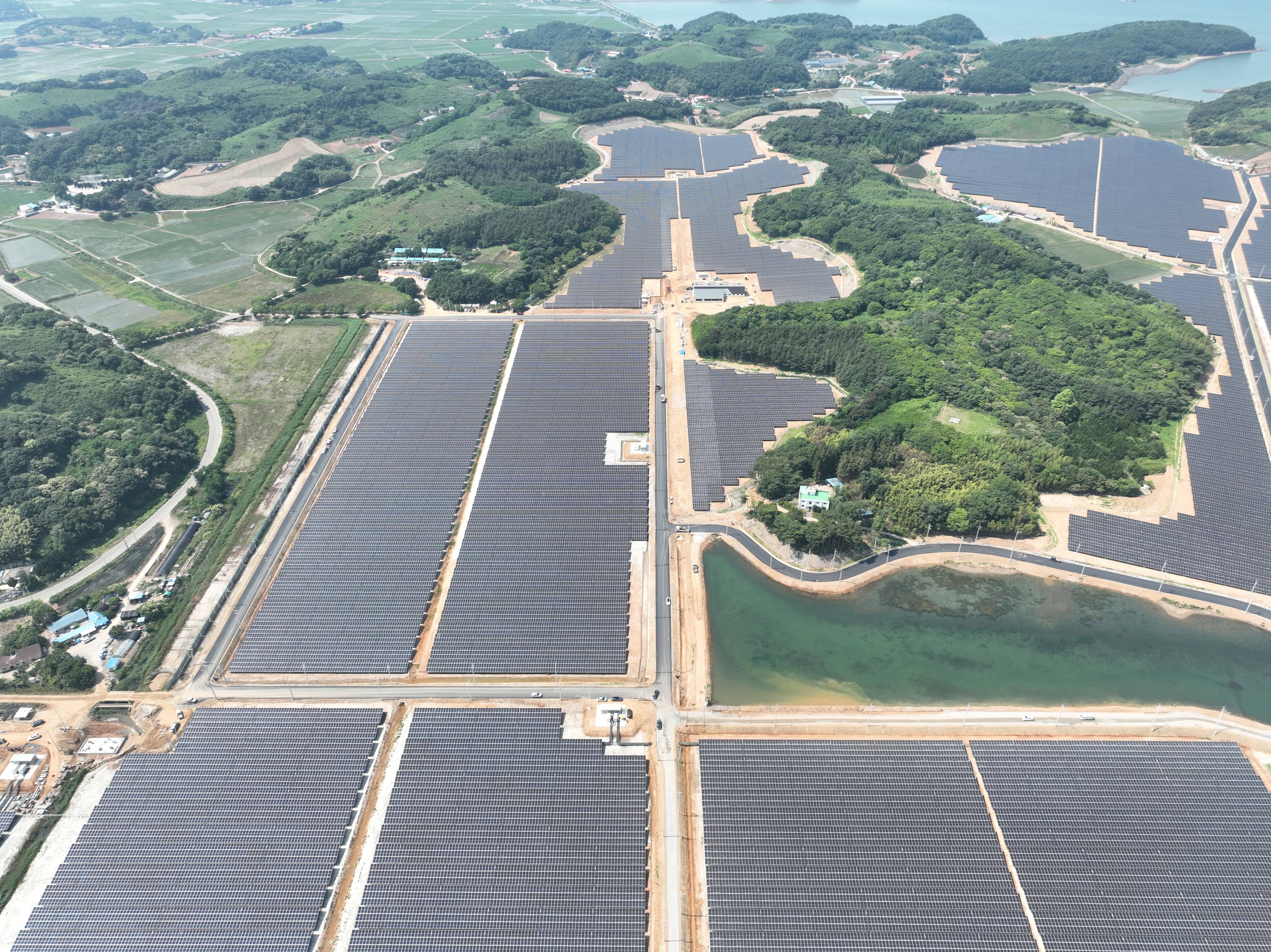 Aerial view of extensive solar panel fields with adjacent greenery, roads, and a small body of water.