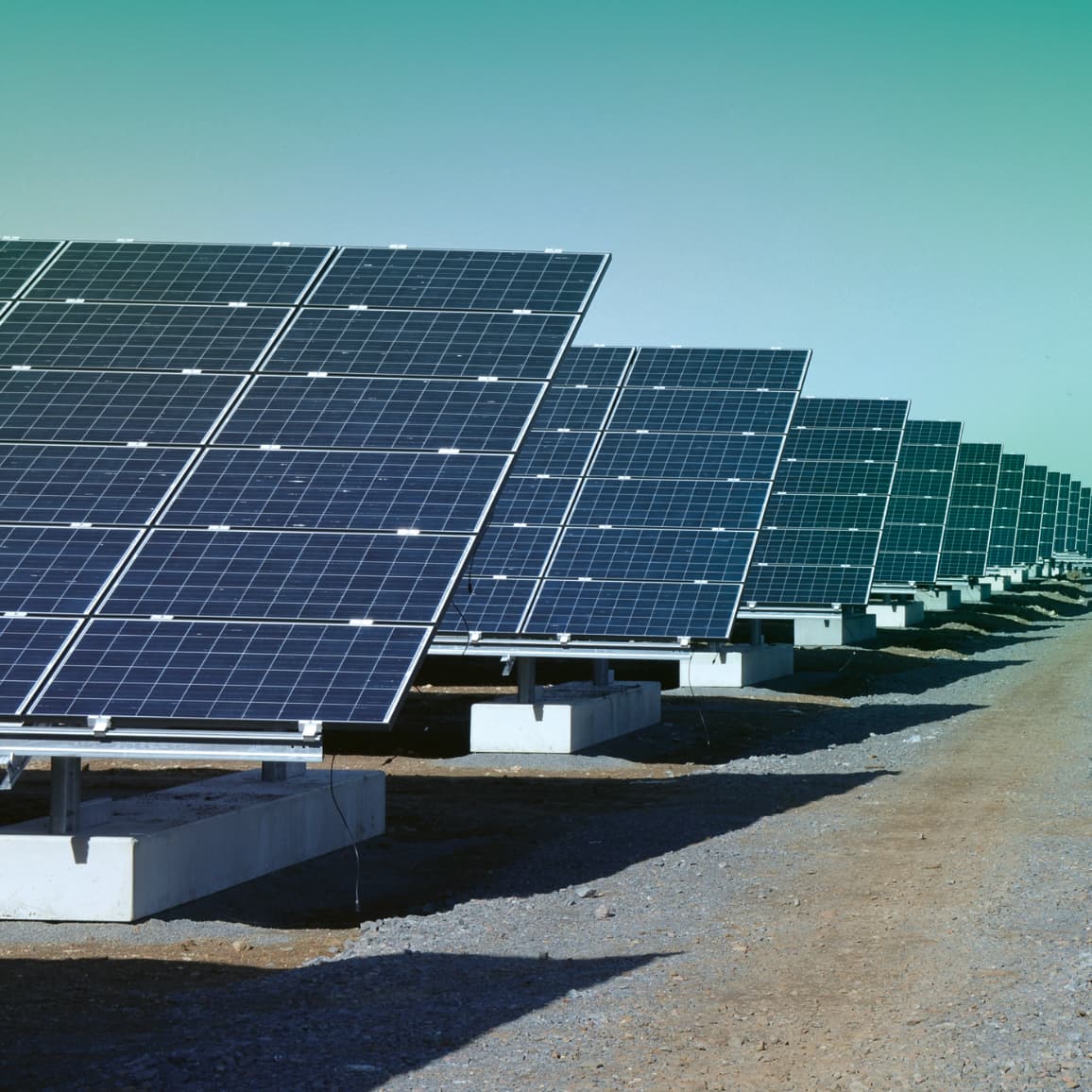 A row of large solar panels installed on the ground in an open area, capturing sunlight for electricity generation, under a clear blue sky.