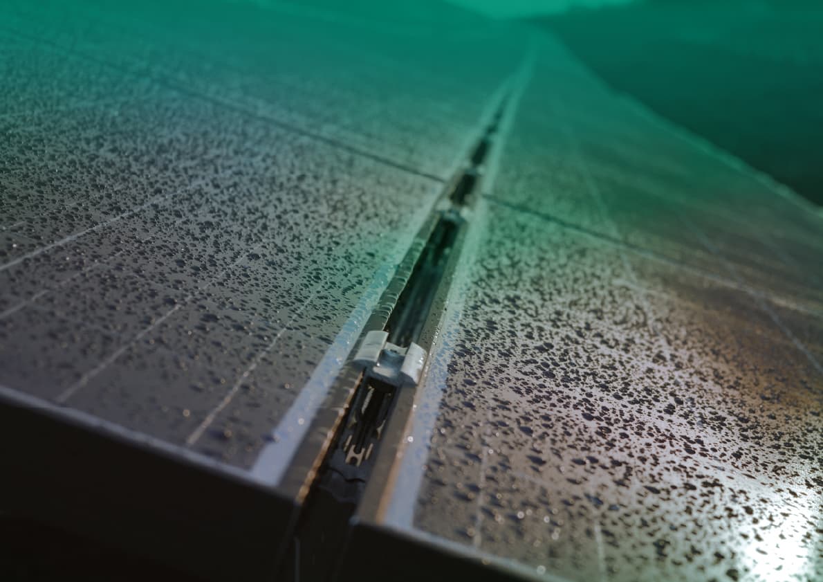 Close-up of a wet, slightly damaged solar panel with droplets of water on its surface against a backdrop of more panels extending into the distance.