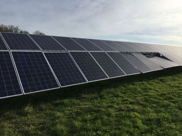 Rows of solar panels installed on a grassy field under a partly cloudy sky.