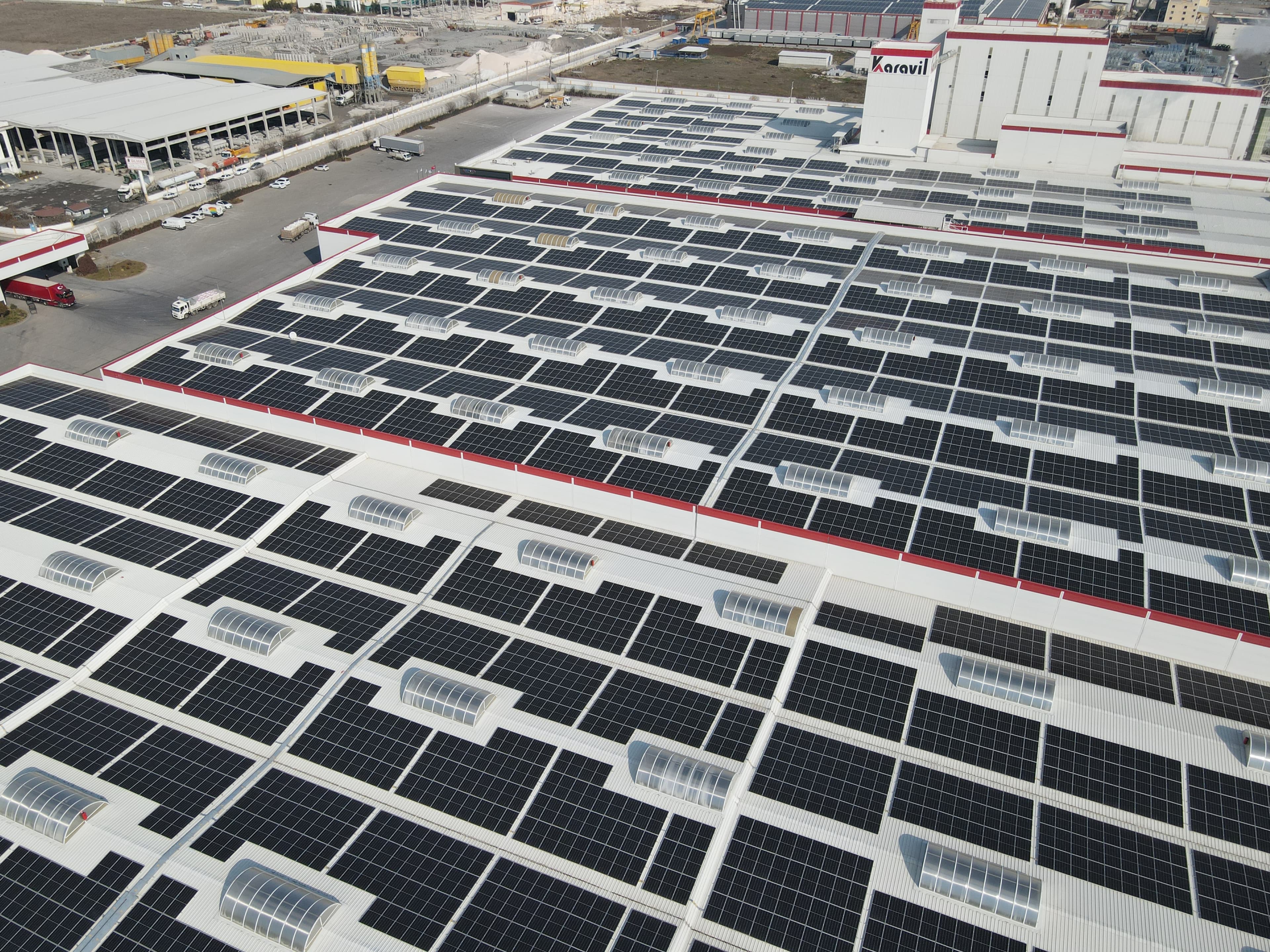Aerial view of large industrial buildings with numerous solar panels installed on their roofs.