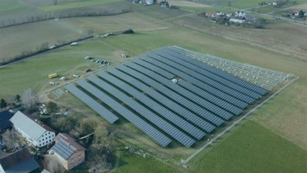 Aerial view of a large solar panel farm in a rural area, surrounded by fields and nearby houses.
